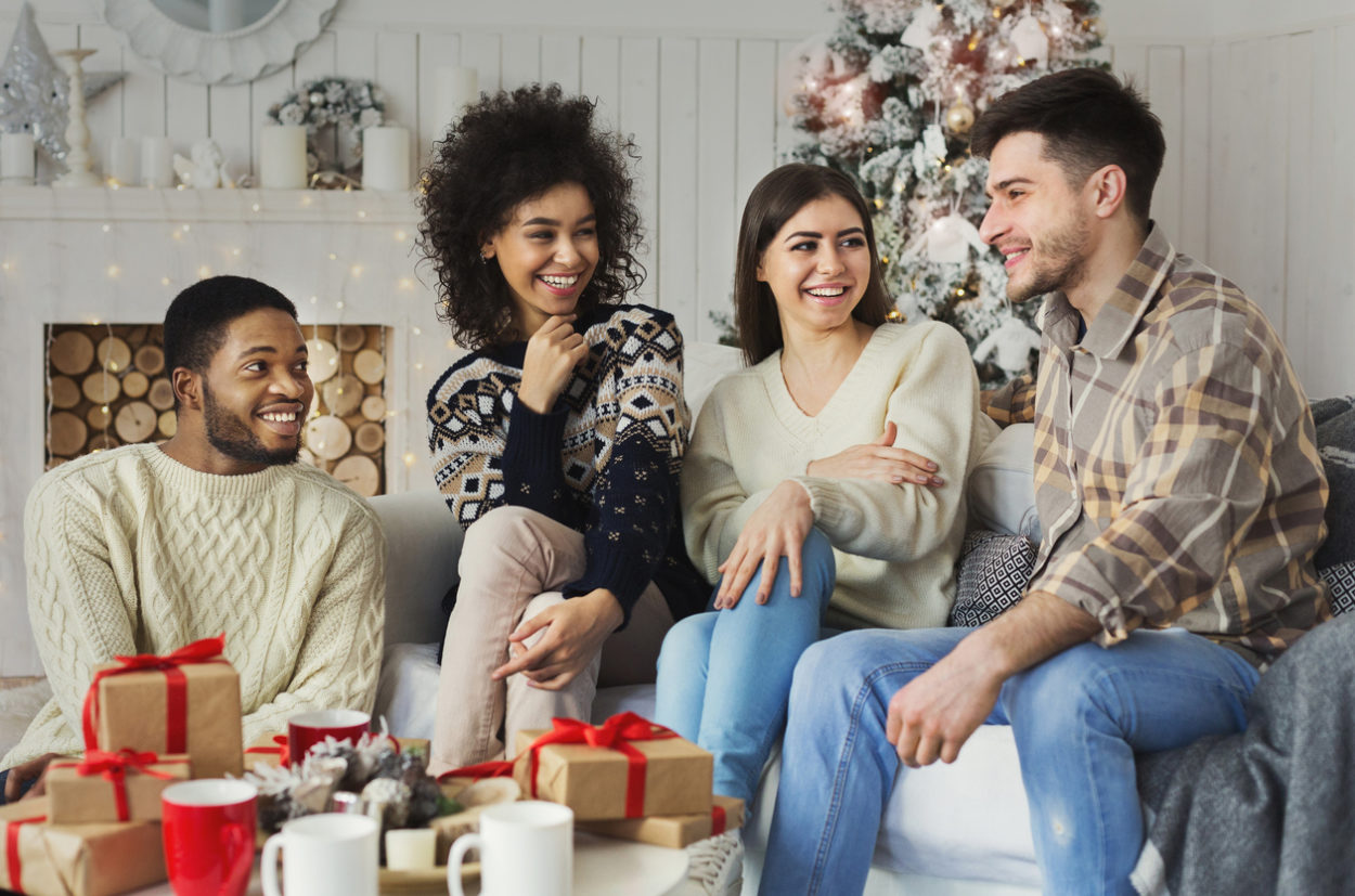 Cheerful friends sitting and talking near new year tree